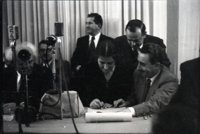 Golda Meir unterzeichnet die Unabhängigkeitserklärung von 1948. Links Ben Gurion. Foto Benno Rothenberg - http://www.archives.gov.il/, Public Domain, https://commons.wikimedia.org/w/index.php?curid=48441234