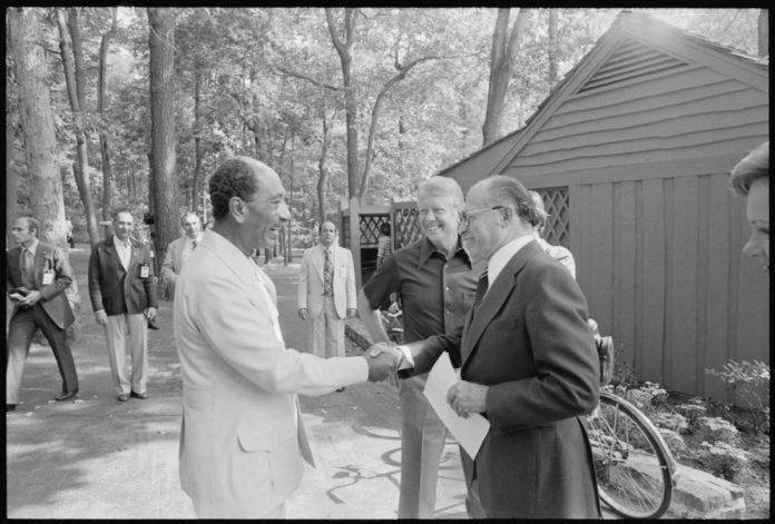 Jimmy Carter beobachtet, wie Anwar Sadat und Menahem Begin sich für eines ihrer Treffen im Camp David begrüssen. Foto U.S. National Archives and Records Administration, Public Domain, https://commons.wikimedia.org/w/index.php?curid=16582502