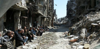 Die 3.903 Palästinenser, die in den letzten sieben Jahren in Syrien getötet wurden, sind für westliche Journalisten und ihre Redakteure nicht von Interesse. Palästinensische Männer sitzen inmitten der Trümmer im Flüchtlingslager Yarmouk, Syrien. Foto UNRWA