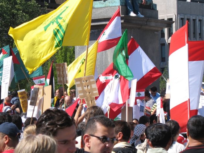 Hisbollah Fahne bei Kundgebung in Stockholm. Foto robotpolisher from Brooklyn, NY, USA - ProtestUploaded by FunkMonk, CC BY-SA 2.0, https://commons.wikimedia.org/w/index.php?curid=14756072
