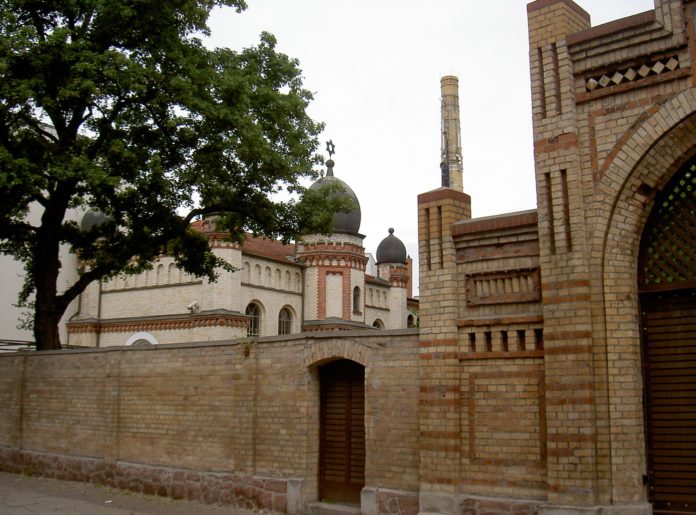 Links im Hintergrund die Synagoge von Halle; im Vordergrund der Eingang zum jüdischen Friedhof. Foto Allexkoch, CC BY-SA 4.0, https://commons.wikimedia.org/w/index.php?curid=42881121