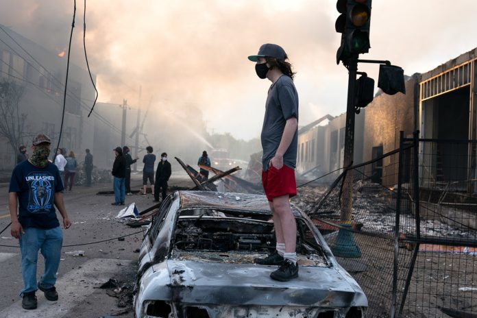 Ausschreitungen in Minneapolis am 28. Mai 2020. Foto Lorie Shaull, St Paul, United States - A man stands on a burned out car on Thursday morning as fires burn behind him in the Lake St area of Minneapolis, Minnesota, CC BY-SA 2.0, https://commons.wikimedia.org/w/index.php?curid=90742413