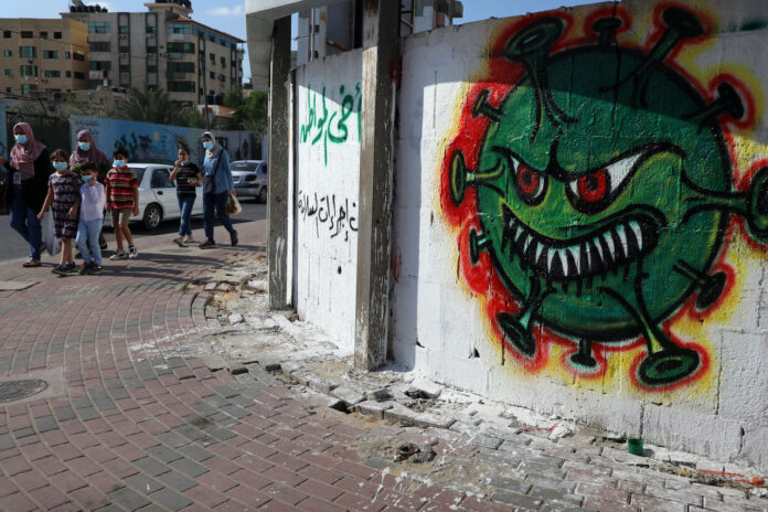 Menschen in Gaza-Stadt gehen an einem Graffiti mit der Darstellung des Coronavirus COVID-19 vorbei. Gaza, 5. Oktober 2020. Foto Majdi Fathi/TPS