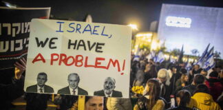 14. Januar 2023, Demonstration in Tel Aviv: Eine Frau hält ein Plakat mit Fotos des israelischen Ministerpräsidenten Benjamin Netanjahu (M), des Justizministers Yariv Levin (L) und des Innenministers Arieh Derei (R) am Habima-Platz in Tel Aviv. Foto IMAGO / ZUMA Wire