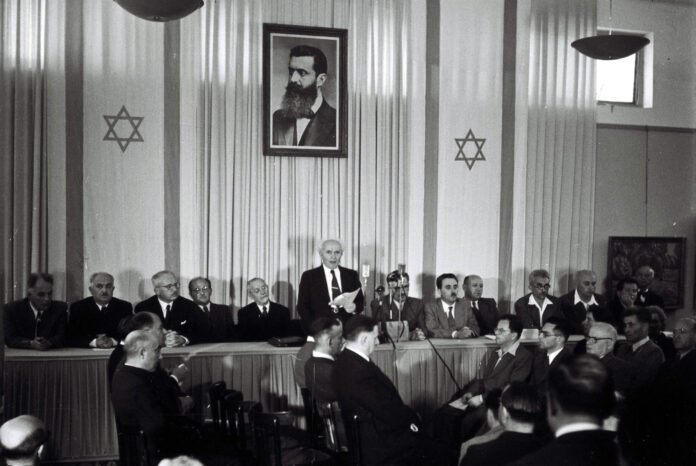 David Ben-Gurion beim Verlesen der Unabhängigkeitserklärungin Tel Aviv. Über ihm das Porträt von Theodor Herzl, dessen Vision eines eigenen Staates für das jüdische Volk rund 50 Jahre später Wirklichkeit wurde. Foto Government Press Office, Israel (GPO)