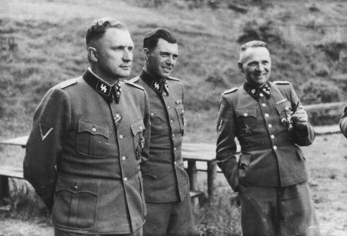 Josef Mengele (Mitte) zwischen den Kommandanten Richard Baer (links) und Rudolf Höß an der Solahütte bei Auschwitz, 1944. Aufnahme aus dem Auschwitz-Album Karl-Friedrich Höckers. Foto USHMM, Gemeinfrei, https://commons.wikimedia.org/w/index.php?curid=65081325 Josef Mengele (Mitte) zwischen den Kommandanten Richard Baer (links) und Rudolf Höß an der Solahütte bei Auschwitz, 1944. Aufnahme aus dem Auschwitz-Album Karl-Friedrich Höckers. Foto USHMM, Gemeinfrei, https://commons.wikimedia.org/w/index.php?curid=65081325